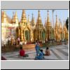 Yangon - Shwedagon Pagode, kleine Pagoden um den Zentralstupa (links unter dem Gerüst) und betende Leute